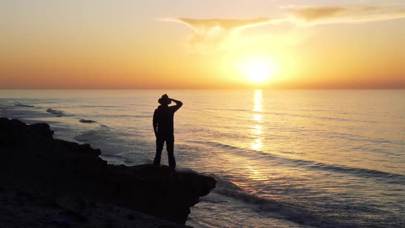 Man in Hat Walk on Rocky Beach and Looking on Beautiful Sunset Sky Above Ocean Landscape Nature