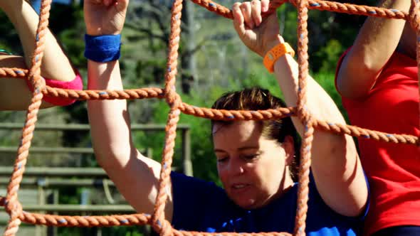 Female trainer assisting women in climbing net during obstacle course