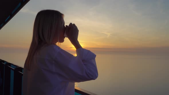 a woman admires the sunset over the sea, and drinks coffee on a high floor.