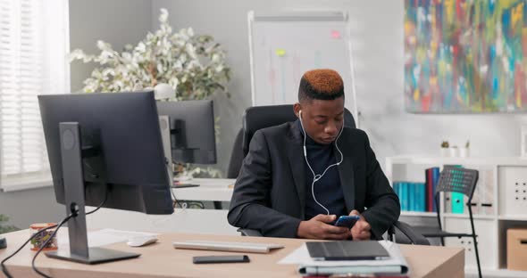 Handsome Man in Suit Sits at Desk in Office No Work Bored Tired Bored Has Headphones in Ears Watches