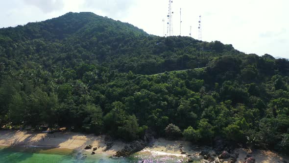 Green hill with lush vegetation, antennas on the top and rocky coastline washed by calm clear water