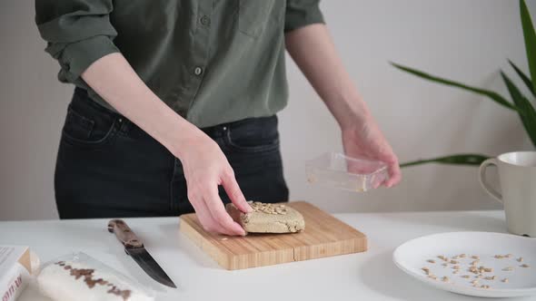 Lady in dark shirt takes delicious brown halva from transparent container and cuts into slices