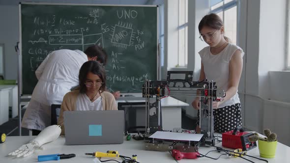 Girl Looks on the 3D Printer and Speaks to the Other Girl