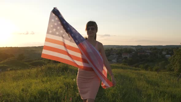 Young woman posing with USA national flag outdoors at sunset. Positive girl celebrating 