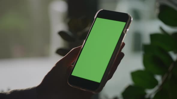Pivoting Around a Hand Holdig a Smart Phone with Green Screen in Shade
