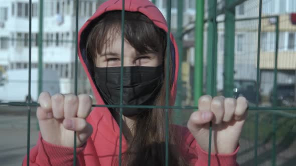 Life in a pandemic. Sad child in a mask behind the fence