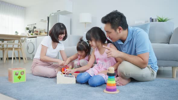 Asian happy family sit on floor, play kid toy together in living room. alt