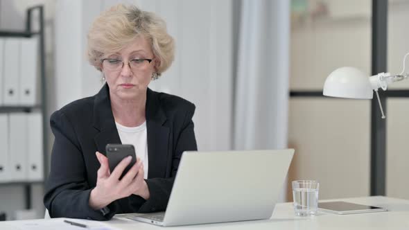 Old Businesswoman Using Smartphone While Working on Laptop