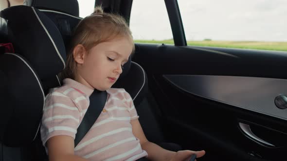 Caucasian girl of 6 years using mobile phone while riding in car. Shot with RED helium camera in 8K.