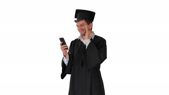Laughing Male Student in Graduation Gown and Mortarboard Having Video Call on His Phone on White