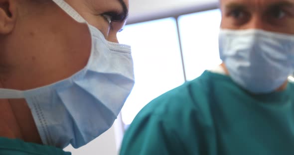 Mixed race male and female surgeons working together in a hospital operating theatre, wearing face m