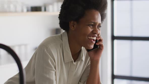 Happy african american woman drinking coffee and talking on smartphone smartphone in kitchen