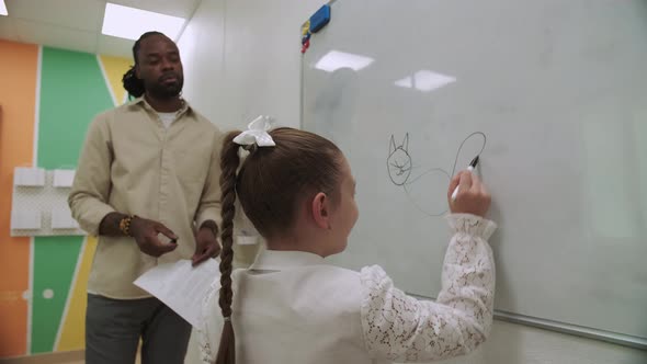 Girl Student Draws Animals on the Chalkboard While the African American Teacher Teaches Her