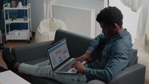 African American Man Working From Home Remote Working on Laptop Computer with Online Graphs and