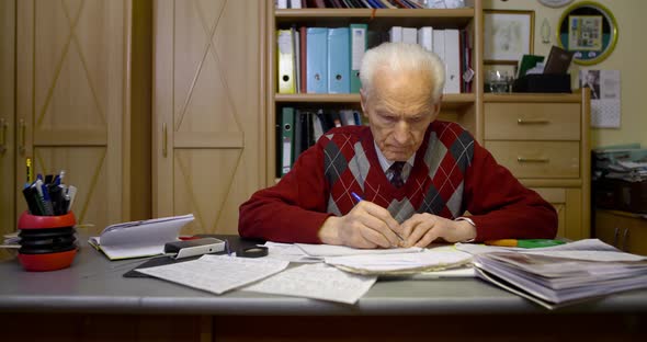 Senior Businessman Writing on Paper at Table in Office