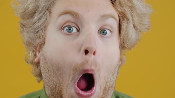 Closeup Portrait of Playful Young Man Making Funny Grimaces Looking at Camera on Yellow Background