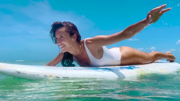 Beautiful Surfer Girl Sitting on Surfboard Smiling In the Water