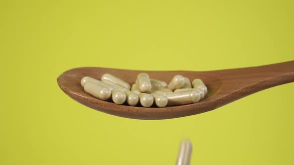 Full wooden spoon with herbal capsules close-up. Falling pills in slow motion