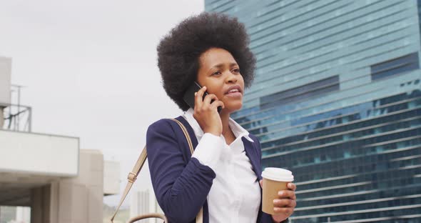 African american businesswoman holding takeaway coffee and talking on smartphone