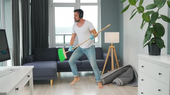 Man in Headphones Cleaning the House and Having Fun Dancing and Singing with a Broom