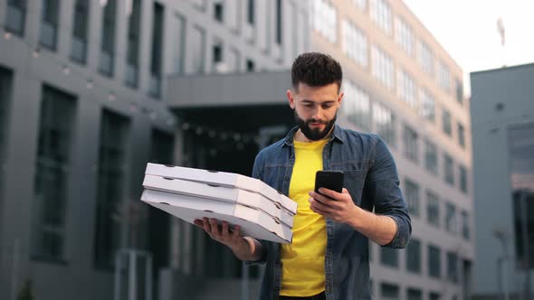 The Food Delivery Guy is Standing and Texting on a Smartphone