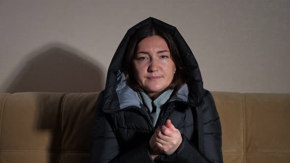 Lady in Warm Jacket with Hood Tries To Heat Hands on Sofa