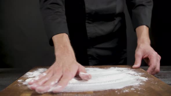 Cook Spreads Flour on Wooden Table on Black Background