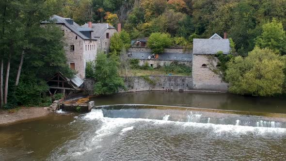 Old stone houses by river dyke among wood, drone pull back