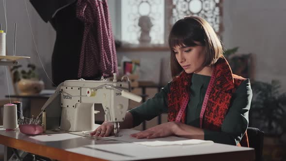 Young Girl In Sewing Studio Sews Behind Sewing Machine