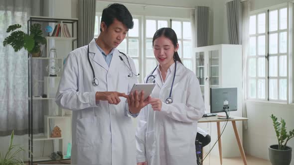 Doctor's Office: Asian Physician Talks With Professional Nurse, Using Tablet Computer alt