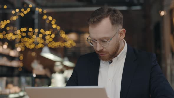 Man Sitting at Table and Working on Laptop at Cafe