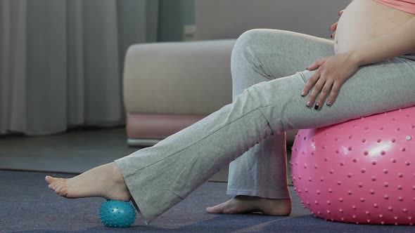 Mother-To-Be Sitting on Fitness Ball, Massaging Feet With Rubber Ball, Body Care