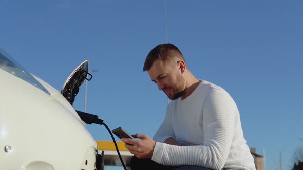 A Male Driver Connects an Electric Car to the Power System to Charge the Car Battery and Controls