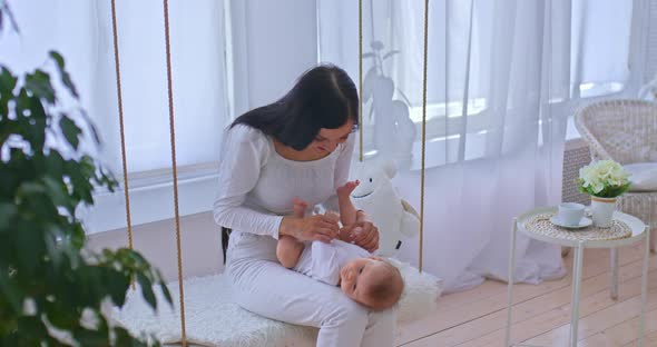 Beautiful Mother Holds the Baby in Her Arms and Sways with Him on a Swing Rocks the Baby