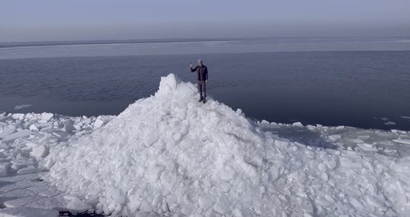 Aerial Dron View of Young Active Happy Man Staying on the Ice Glaciers Near Coastline of Winter Sea