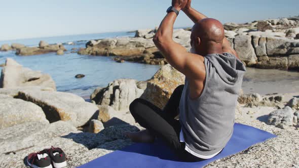 Senior african american man exercising stretching on rocks by the sea