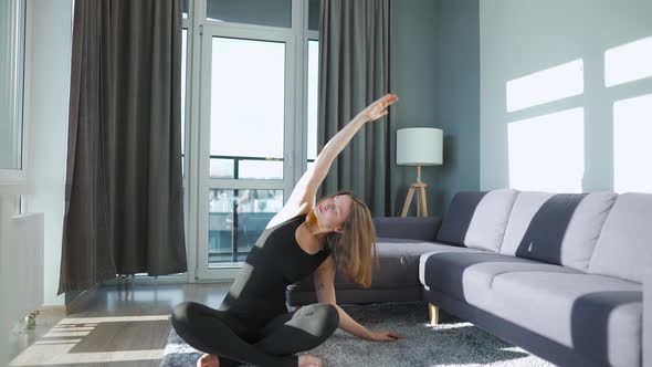 Young Caucasian Woman in Black Jumpsuit Doing Yoga at Home to Develop Flexibility and Balance