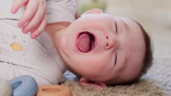 A happy child sneezes lying on the carpet in the home room, age eight months. Toddler baby boy smile