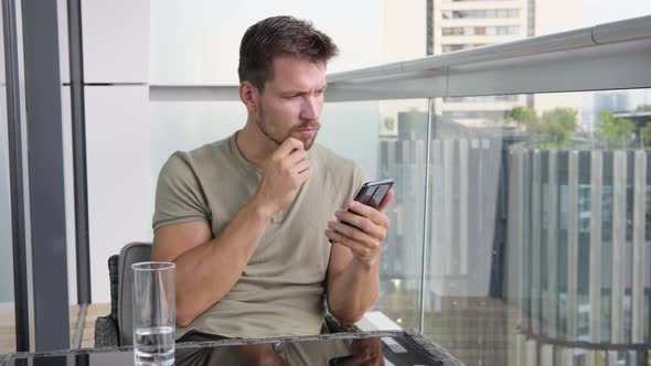 A Young Handsome Man Works on a Smartphone As He Sits on a Balcony in a Luxurious Apartment