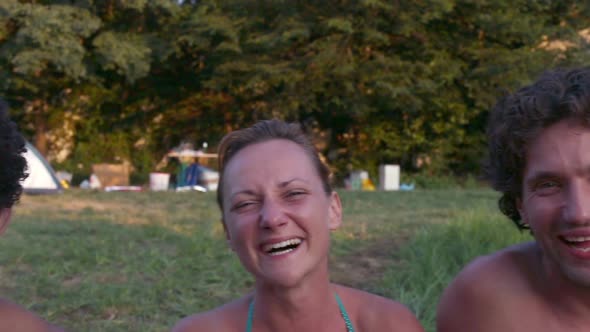 Portrait of group of friends sitting in nature at sunset, laughing at camera