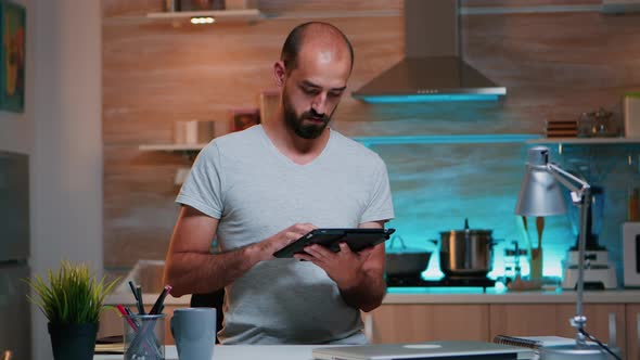 Man Typing on Tablet Working From Home at Night