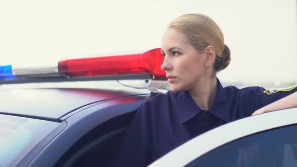 Concentrated Female Officer Monitoring Road Situation Standing Near Police Car