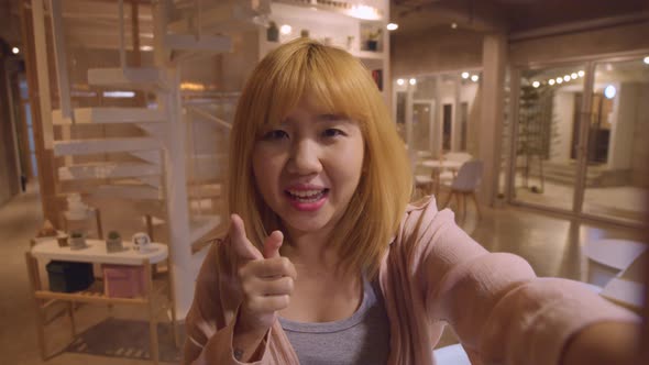Asian friendly women influencer waving hand looking at camera at night cafe.