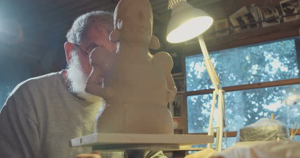 Old sculptor working on a clay sculpture in his small studio