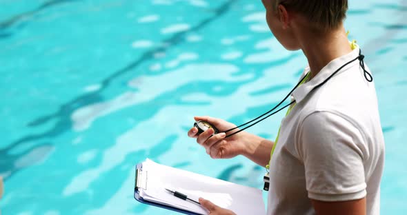 Swimming coach holding clipboard and looking at stopwatch