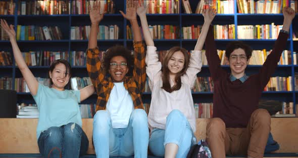 Portrait of Happy Diverse Students Raising Hands and Smiling at Camera in Library