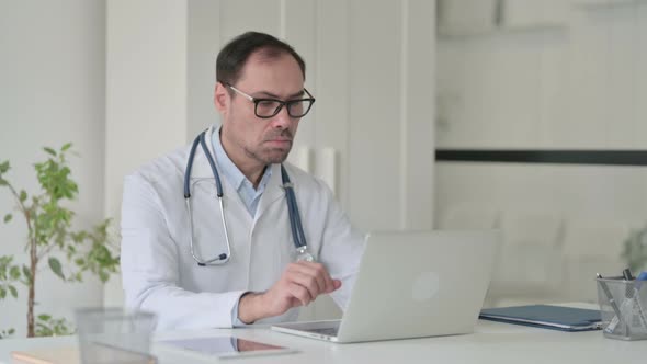 Middle Aged Doctor with Laptop Looking at the Camera in Office