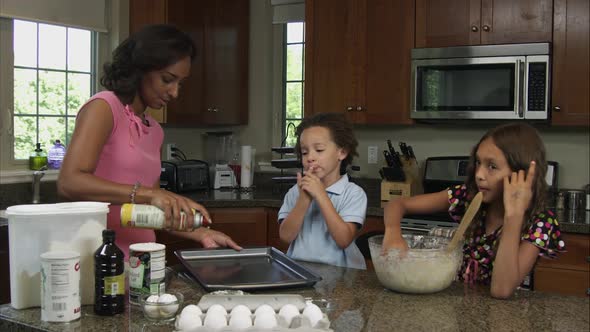 Slow motion of mother spraying non stick can onto cookie sheet.