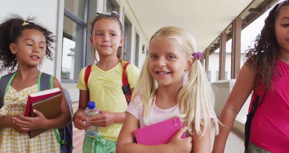 Video of happy diverse girls walking at school corridor and talking