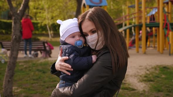 Portrait of a Mother in a Medical Mask with a Small Child in the Park. Covid-19